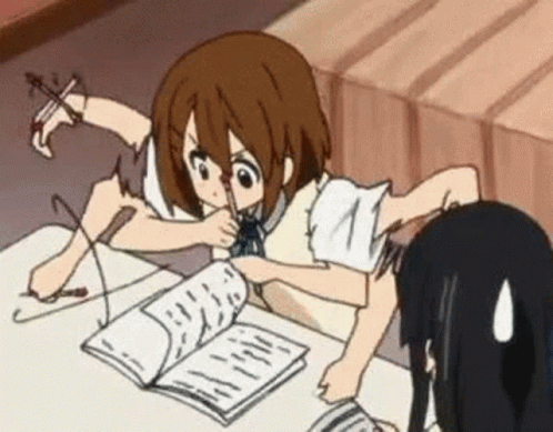 Girl studying at desk with book, hand moving, another person's back visible.