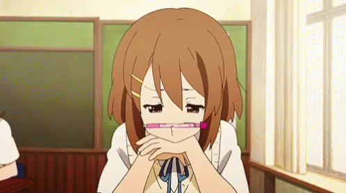Girl with glasses sitting at desk, blinking slowly with hands under chin.