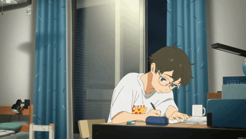 Young man studying at desk, looking up thoughtfully from laptop.