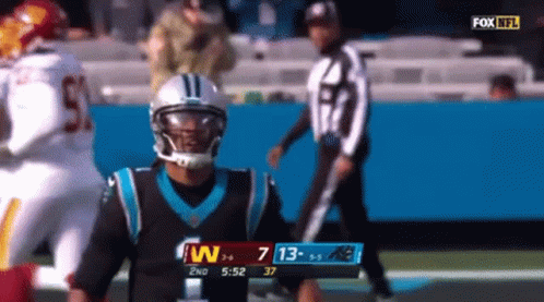 Football player fumbles the ball and looks down at the ground.