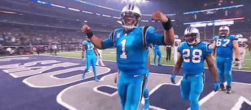 Football player in blue uniform walking and pointing forward on field.