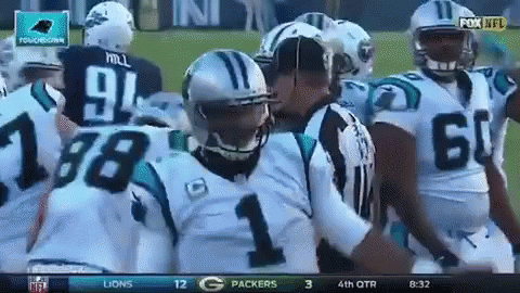 Football player fumbles ball during game, teammates and opponents around him.