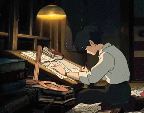 Young man drawing at a desk under a lamp in a dark room.