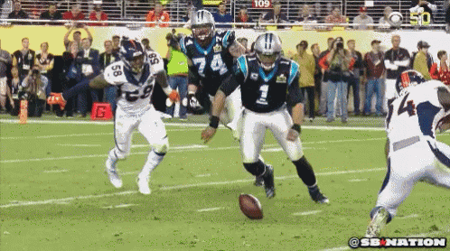 Football player fumbles ball, tackled by multiple players on field.