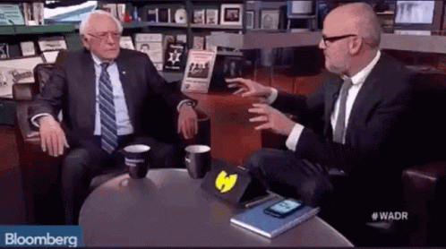 Man in suit gesturing and touching face while speaking in interview setting.