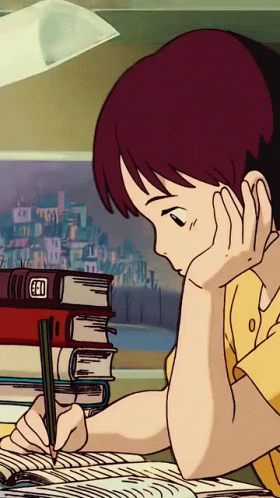 A student studying at a desk with books and papers, wearing headphones and writing.